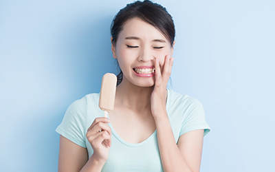 A woman holding an ice cream bar while holding her jaw in pain